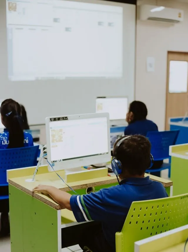 Children engaged in learning at a computer lab, using computers in a classroom setting.